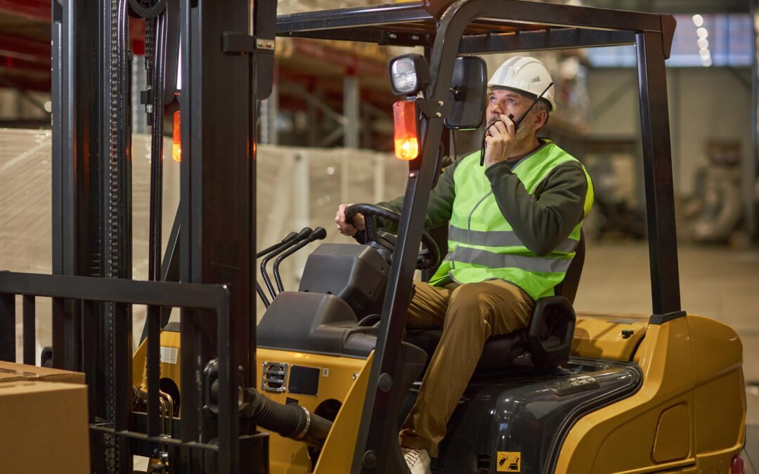 Side View Of A Man Talking On A Walkie Talkie While Sitting In A Forklift | Brennan Equipment Services